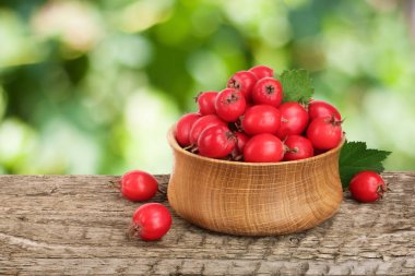 Hawthorn berry yaprak bulanık bir bahçe arka plan ile ahşap masa üzerinde bir kase ile
