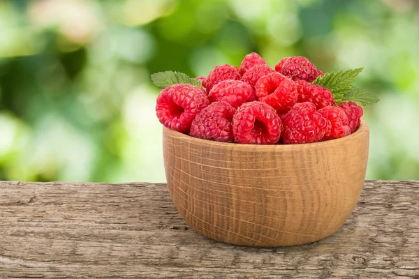 Ahududu bulanık bir bahçe arka plan ile tabloda bir ahşap kase