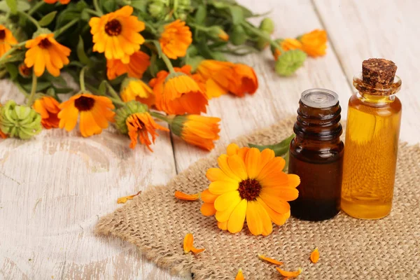 Aceite esencial de aromaterapia con flores frescas de caléndula sobre fondo de madera blanca. Aceite de caléndula — Foto de Stock