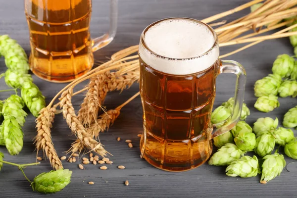 Склянка пінистого пива з шишками хмелю та пшениці на чорному дерев'яному фоні — стокове фото