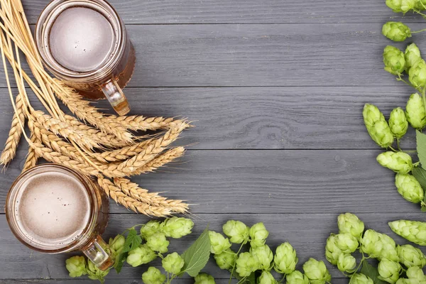 glass of foamy beer with hop cones and wheat on black wooden background. Top view with copy space for your text