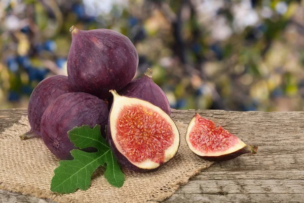 Fig fruits with leaves on old wooden board with blurred garden background — Stock Photo, Image