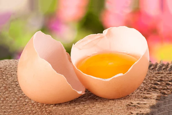 Uovo rotto con tuorlo e guscio d'uovo Su un tavolo di legno con uno sfondo sfocato giardino — Foto Stock