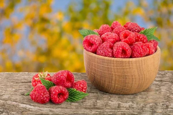 Ahududu bulanık bir bahçe arka plan ile tabloda bir ahşap kase