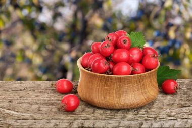 Hawthorn berry yaprak bulanık bir bahçe arka plan ile ahşap masa üzerinde bir kase ile