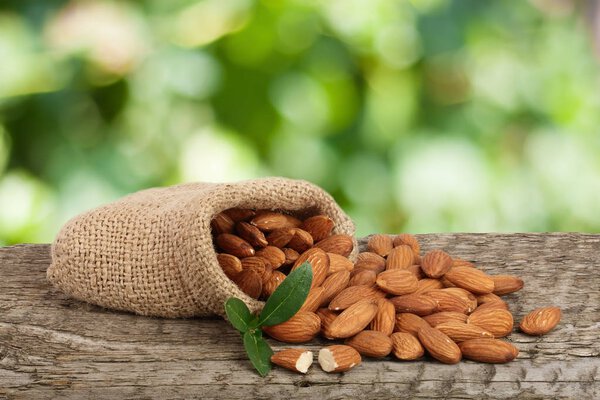 Almonds with leaf in bag from sacking on a wooden table with blurred garden background