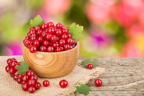 Красная смородина ягоды в деревянной чаше на деревянном столе с размытым фоне сада — стоковое фото
