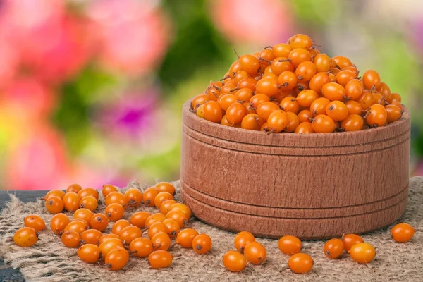 Sanddornbeeren in einer hölzernen Schüssel auf dem Tisch mit verschwommenem Gartenhintergrund — Stockfoto