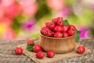 Hawthorn berry yaprak bulanık bir bahçe arka plan ile ahşap masa üzerinde bir kase ile