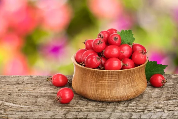 Hawthorn berry z liści w misce na drewnianym stole z niewyraźne tło ogród — Zdjęcie stockowe