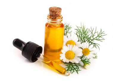 Beyaz arka planda özgün yağ ve taze papatya çiçekleri bulunan şişe.