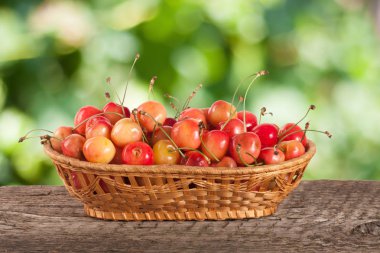 Bulanık bir bahçe arka plan ile ahşap bir masa üzerinde bir hasır sepet içinde sarı kiraz