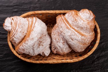 iki ay çöreği siyah taş arka plan üzerinde bir hasır sepet içinde pudra şekeri serpilir. Üstten Görünüm
