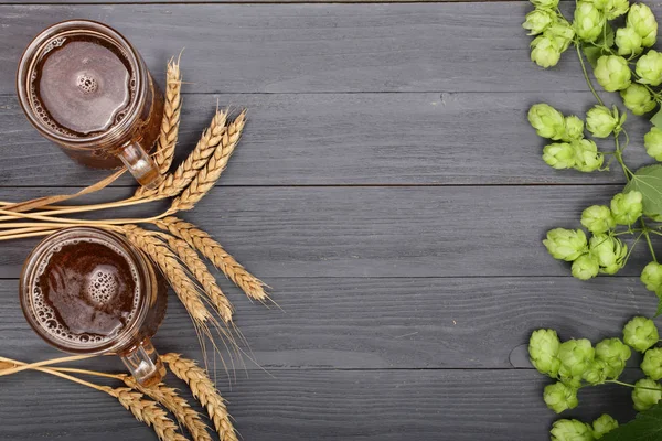 Склянка пінистого пива з шишками хмелю та пшениці на чорному дерев'яному фоні. Вид зверху з пробілом для копіювання вашого тексту — стокове фото