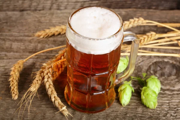 Glas schuimend bier met hopbellen en tarwe op oude houten achtergrond — Stockfoto