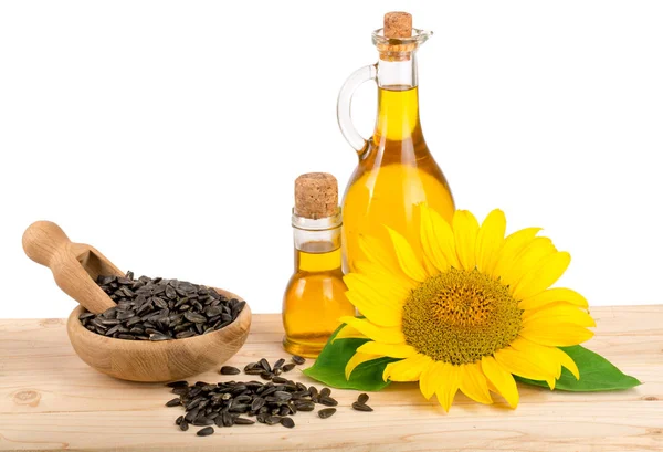 Подсолнечное масло, семена и цветок на деревянном столе на белом фоне — стоковое фото