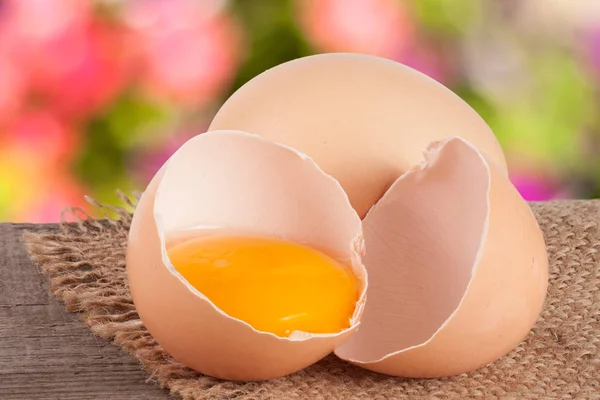 Broken egg with yolk and eggshell On a wooden table with a blurry garden background — Stock Photo, Image