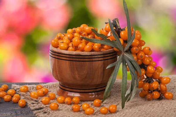 Sanddornbeeren in einer hölzernen Schüssel auf dem Tisch mit verschwommenem Gartenhintergrund — Stockfoto