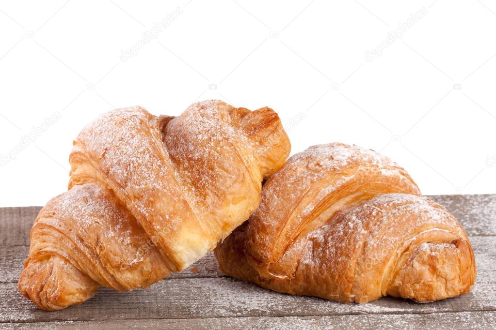 two croissant sprinkled with powdered sugar on a wooden table with white background