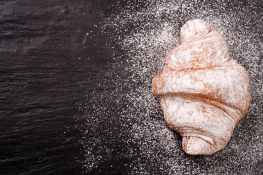 bir kruvasan kopya alanı metni siyah taş zemin üzerine pudra şekeri serpilir. Üstten Görünüm