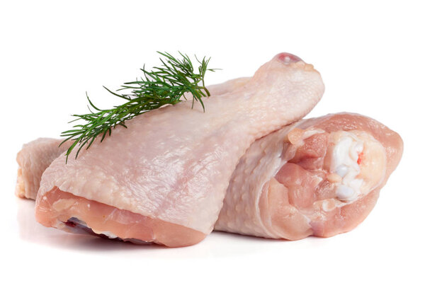 Two raw chicken drumsticks with a sprig of dill isolated on white background