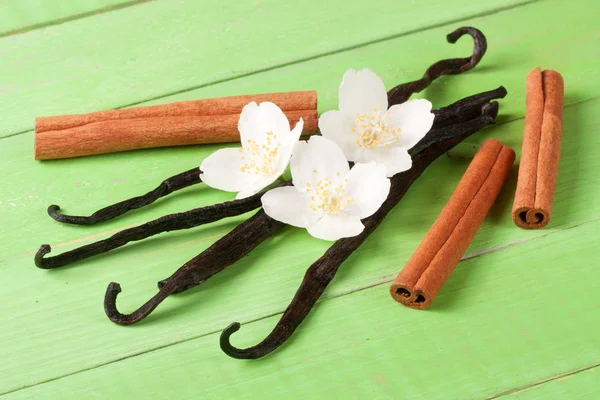 Stik vanili dan kayu manis dengan bunga dan daun pada latar belakang kayu hijau — Stok Foto