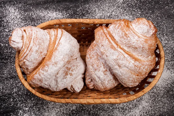 Två croissant beströdda med florsocker i en korg på svart sten bakgrund närbild. Ovanifrån — Stockfoto