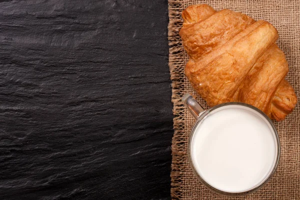 Pohár tej, croissant-t, a fekete kő háttér, a szöveg másolása szóközzel. Szemközti nézet — Stock Fotó