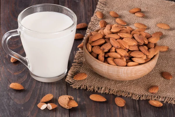 Lait d'amande dans un verre et amandes dans un bol sur fond de bois foncé — Photo