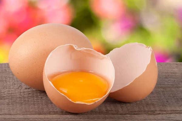 Gebroken ei met eigeel en de "eggshell" op een houten tafel met een wazige achtergrond van tuin — Stockfoto