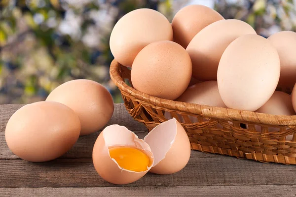 Eieren in een rieten mand op een houten bord met onscherpe achtergrond van de tuin — Stockfoto