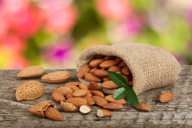 Almonds with leaf in bag from sacking on a wooden table with blurred garden background clipart
