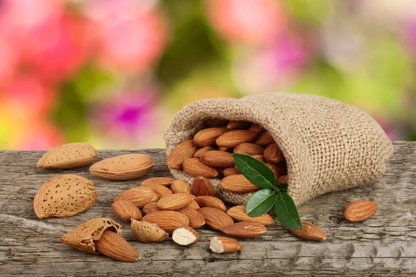 Mandlar med blad i väska från plundringen på ett träbord med suddig trädgård bakgrund — Stockfoto