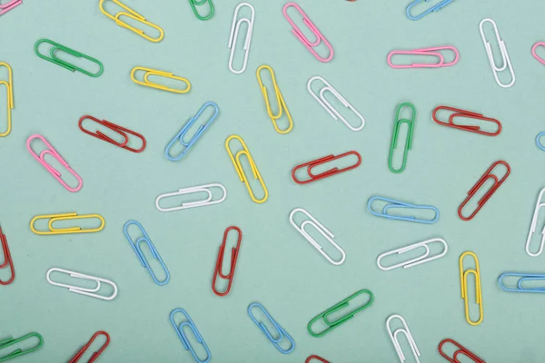 colorful paper clips on green background. Top view. Flat lay pattern
