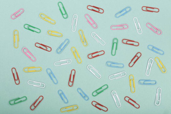 colorful paper clips on green background. Top view. Flat lay pattern