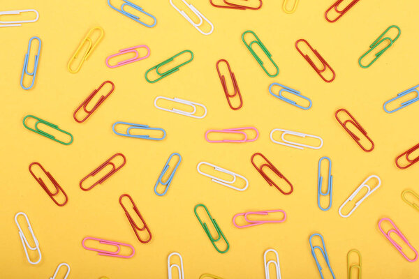 colorful paper clips on yellow background. Top view. Flat lay pattern