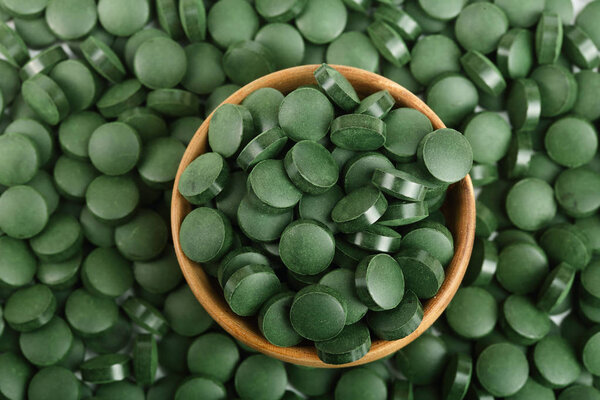 heap of Spirulina tablets algae nutritional supplement in wooden bowl as a background close up top view. Flat lay