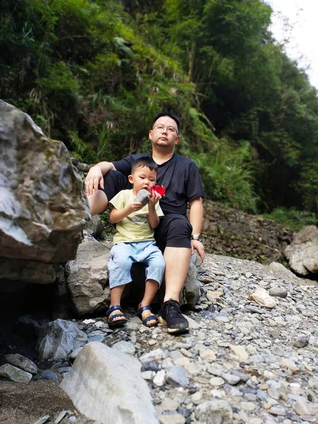 father and son sitting on the rocks in the forest