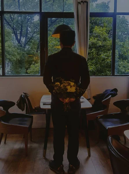 man in a black suit with a laptop in the background of the window