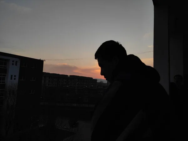 silhouette of a man in a black jacket and a white shirt on the roof of the building