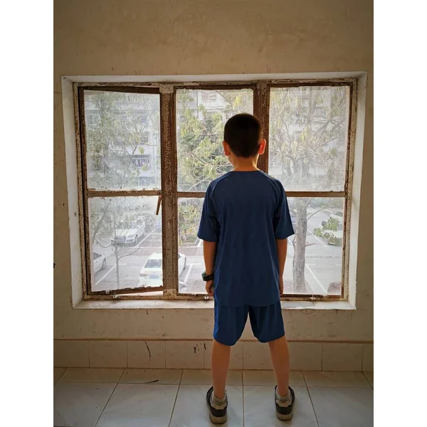 boy in a white t-shirt standing near the window