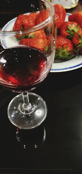 glass of red wine with ice and strawberries on a black background