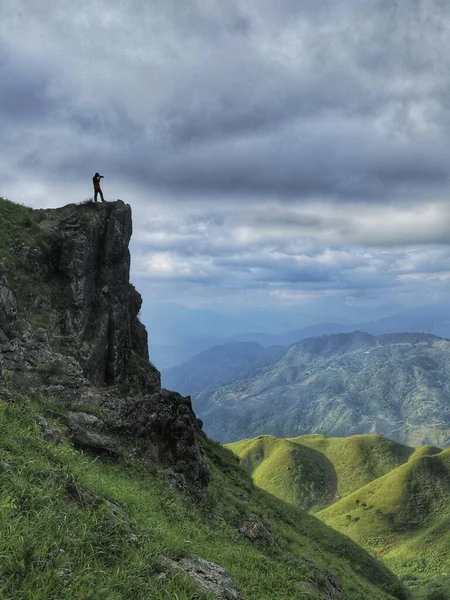 a man in a green jacket is standing on a mountain top