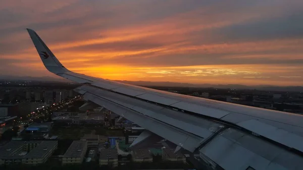 airplane flying above window at sunset