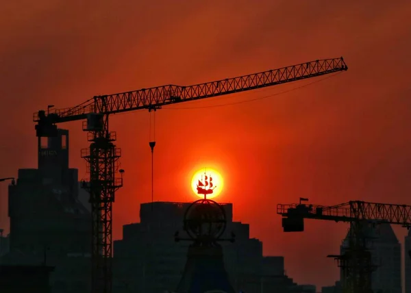 silhouette of a building with a crane and a red sunset