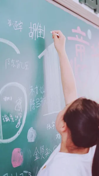 young female teacher writing on blackboard