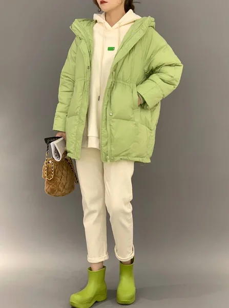 fashion model in a green jacket and a yellow sweater and a black bag on a beige background.