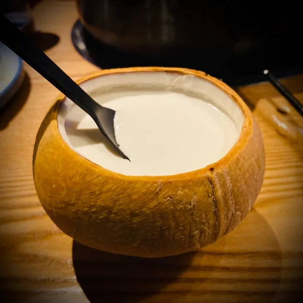 a closeup shot of a coconut milk with a spoon and a cup of tea