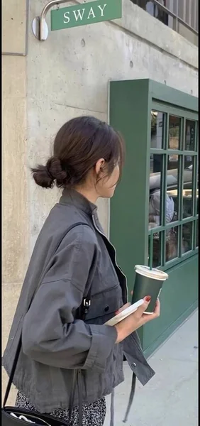 young woman in a white shirt and a black jacket is standing in the street with a cup of coffee