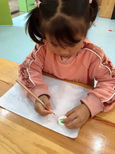 little girl draws a paper with a pencil on the table